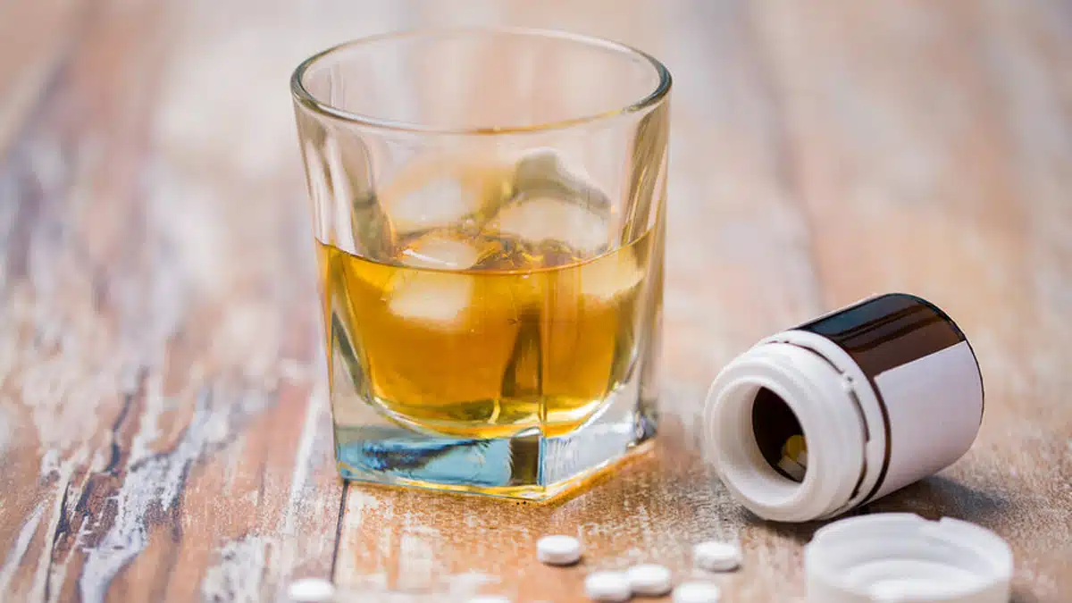 A glass of alcohol next to an open bottle of pills on a table