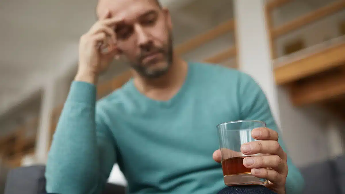 Woman with her head in her hands and a glass of wine. Graphic explains why detox is necessary for addiction recovery.