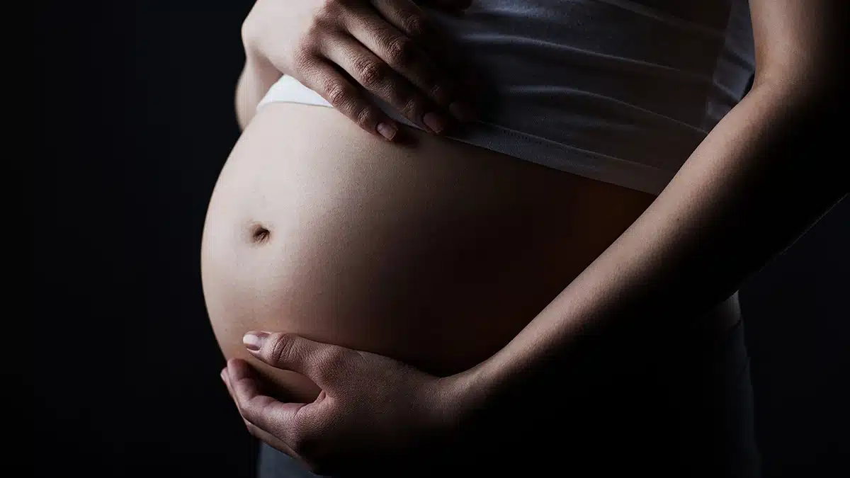 Closeup of pregnant woman’s stomach. Text explains how a small amount of alcohol can harm a developing fetus