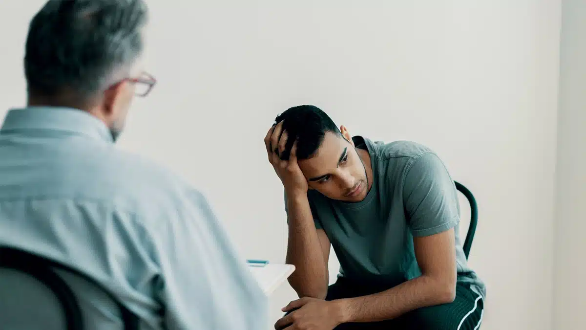 Man holding his head meeting with male therapist. Addiction impairs decision making, emotional control, and self regulation.