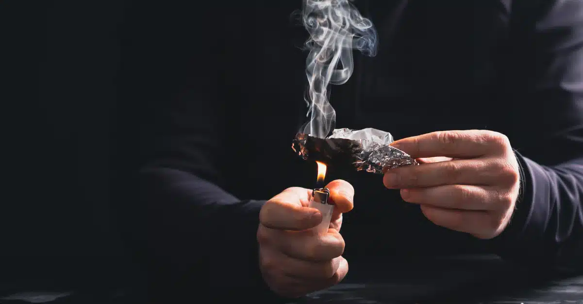 Man holding meth one hand an lighting it up with a lighter in the other.