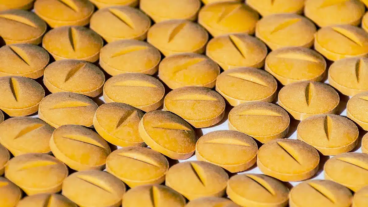 A close-up view of numerous round, yellow tablets, each with a groove in the middle, arranged in a grid pattern