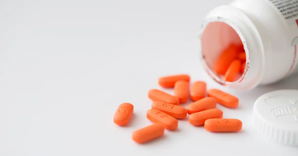 A white prescription bottle lies on its side, with several orange pills spilling out onto a white surface.